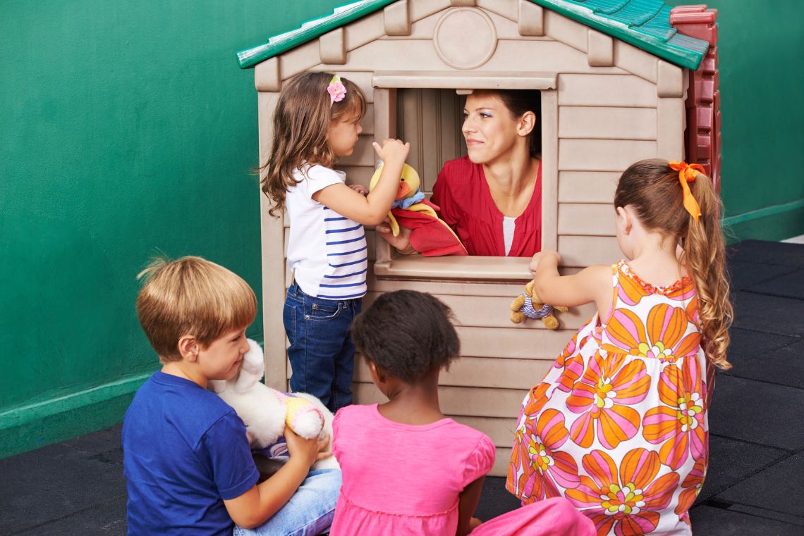 Gruppe Kinder sitzt bei Puppentheater im Kindergarten vor einem Spielhaus